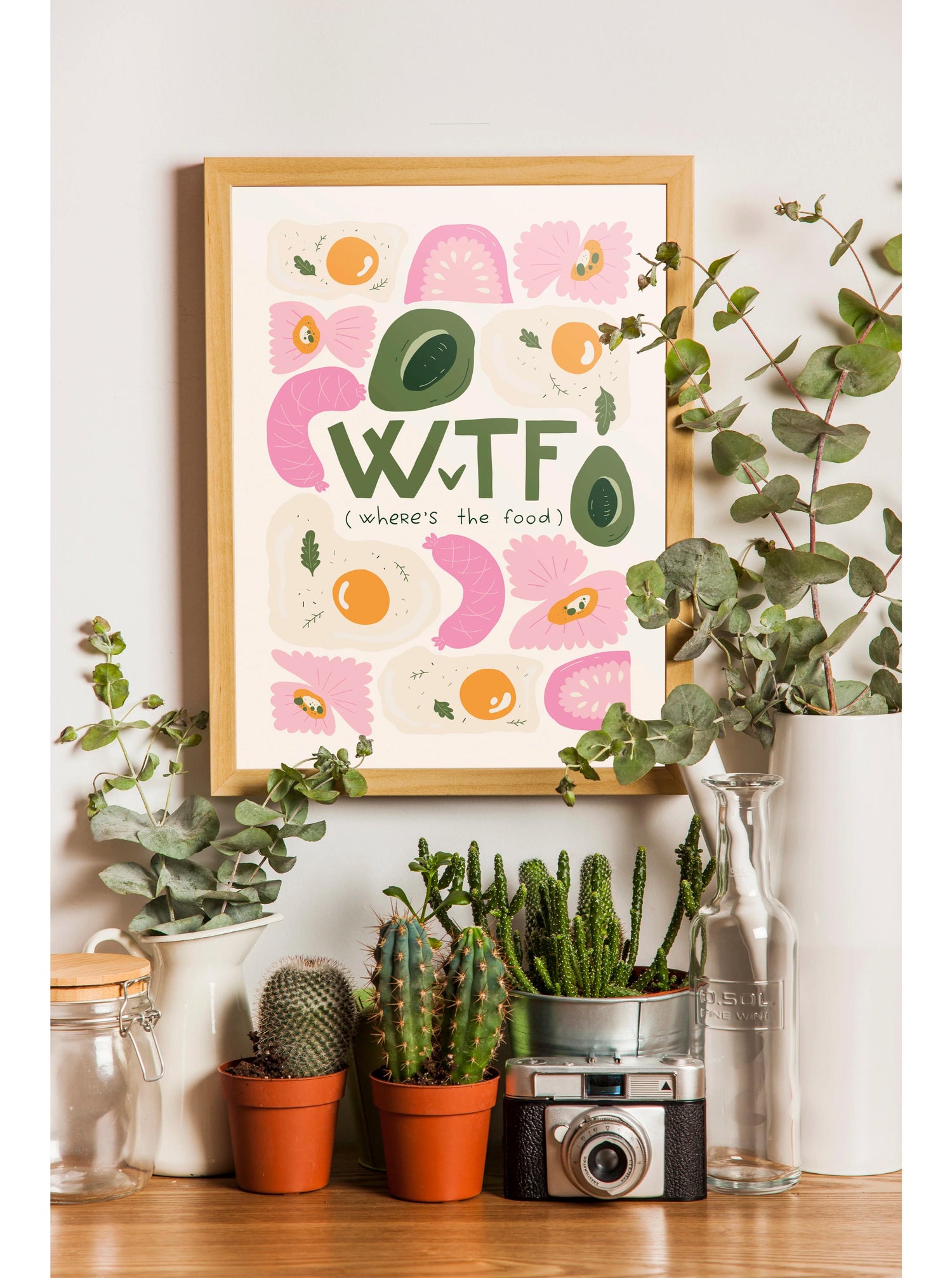 a framed poster with a playful message, surrounded by various potted plants and a vintage camera on a shelf.