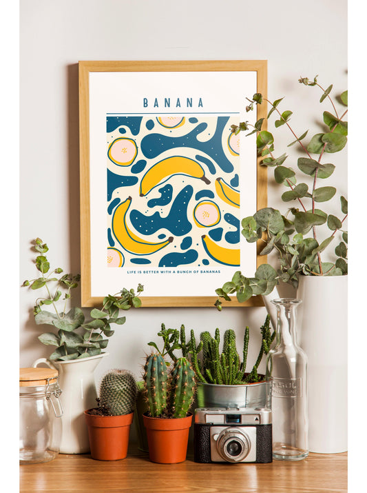 a framed poster of bananas, surrounded by various potted plants and a camera on a wooden surface.